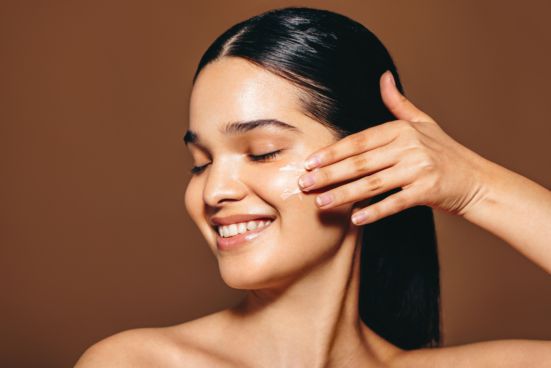 Happy with her skincare routine: Woman in her 20’s applies beauty cream on her face